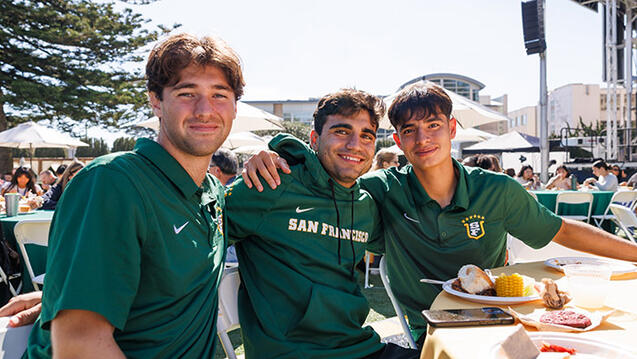 Students sitting around a table outside eating barbecue