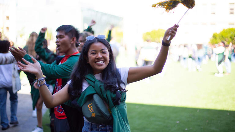 A student smiling and waving a USF spirit pom pom in the air