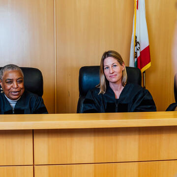 Two judges behind their desk speak to a student in moot court.