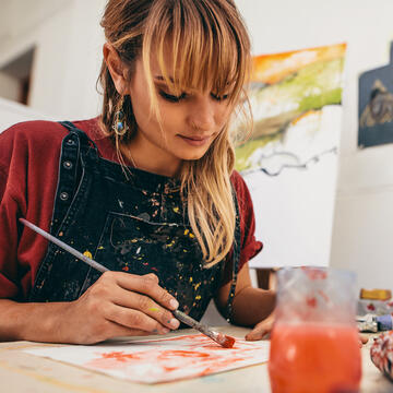 Person painting at a table wearing a paint-splattered apron
