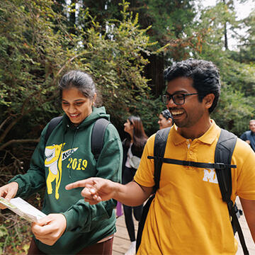 Two students smiling and pointing at a map in Muir Woods