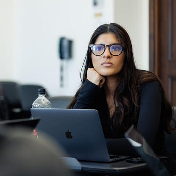 Student with glasses sitting at desk, paying attention to classmate