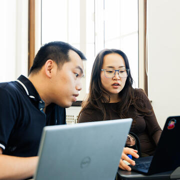 two students look at laptops together in class